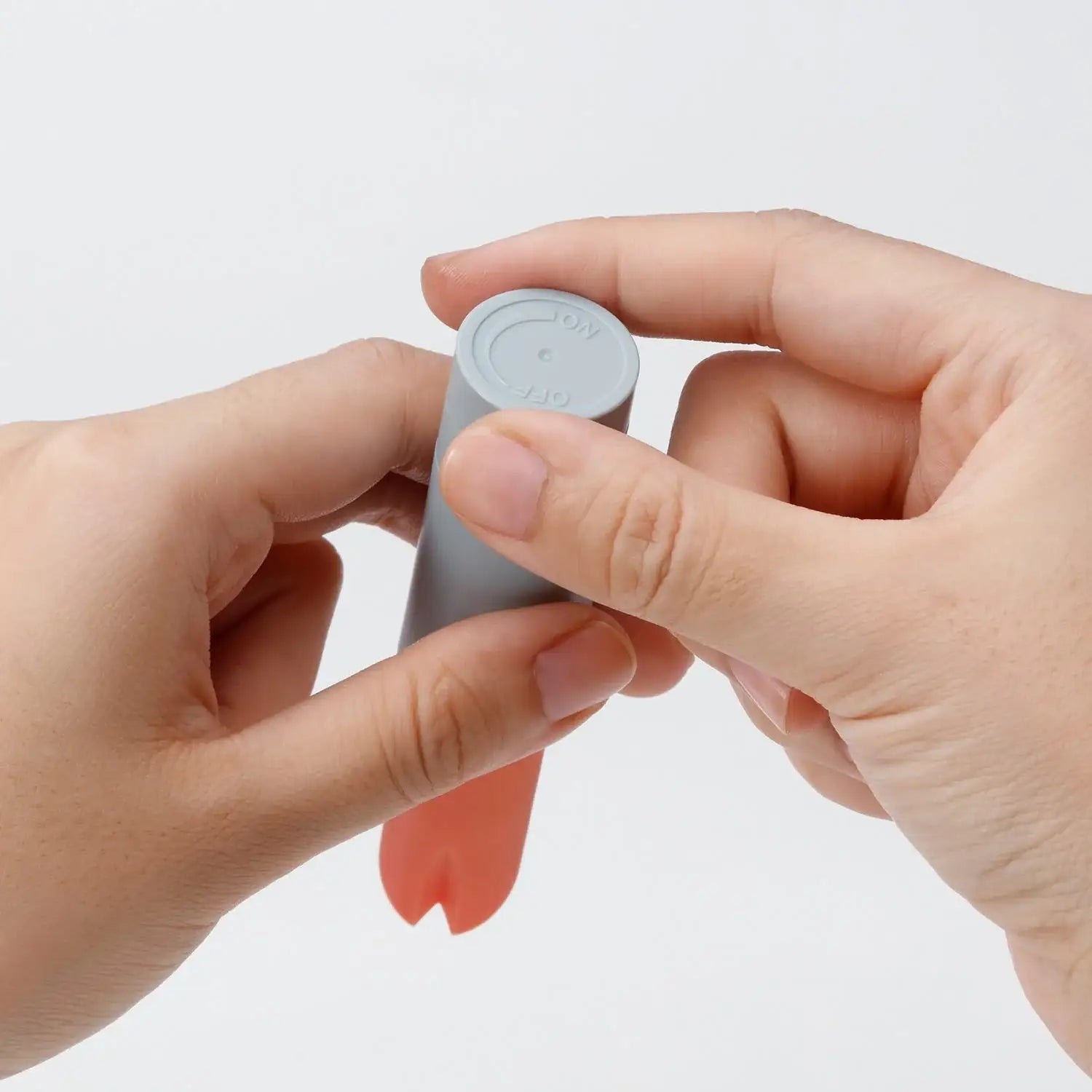 Close-up of hands holding a small cylindrical object with a pink component on a white background
