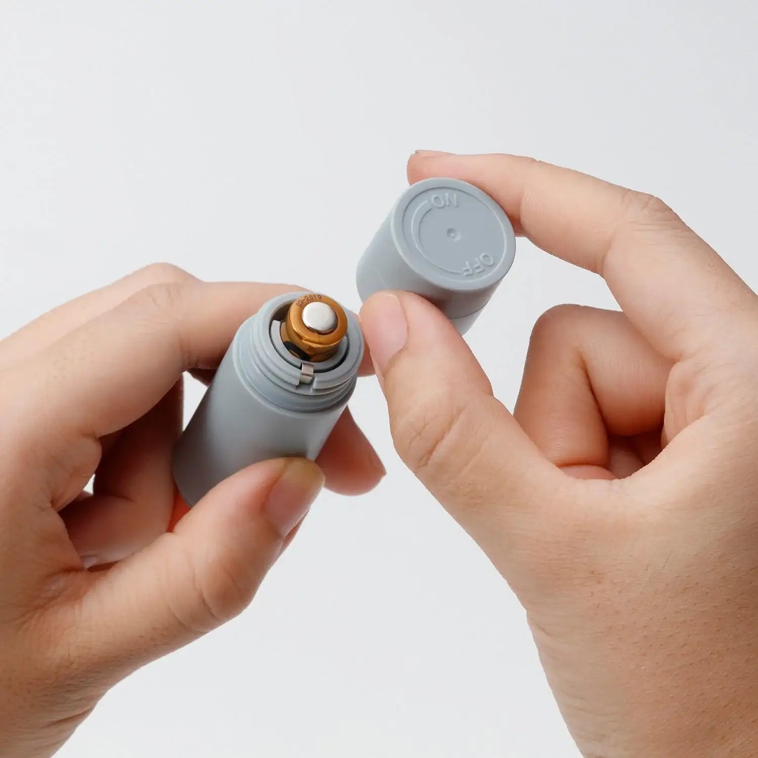 Close-up of hands holding a small cylindrical device with a cap, on a light gray background