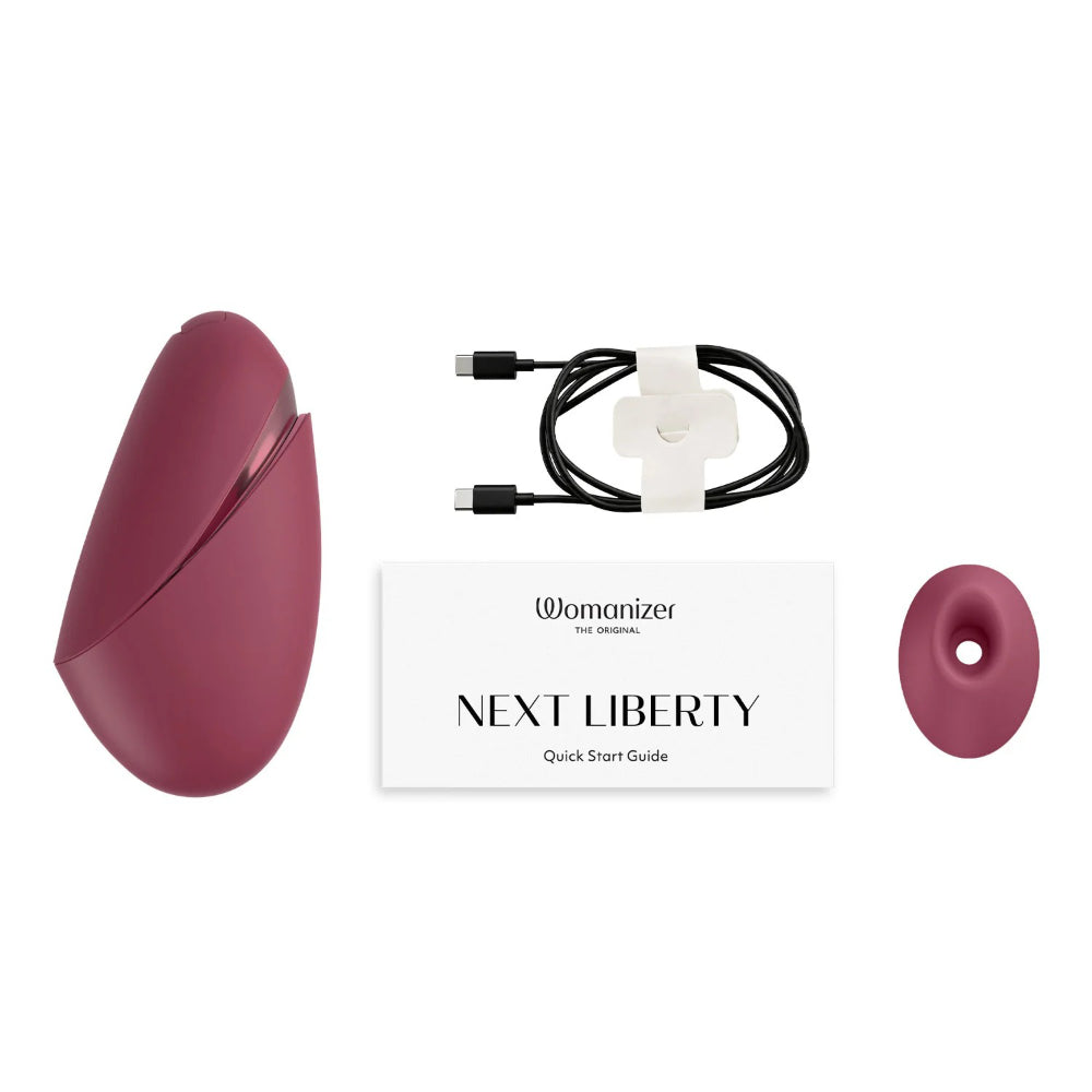 Womanizer Next Liberty with magnetic charging cable and interchangeable stimulation head accessories.