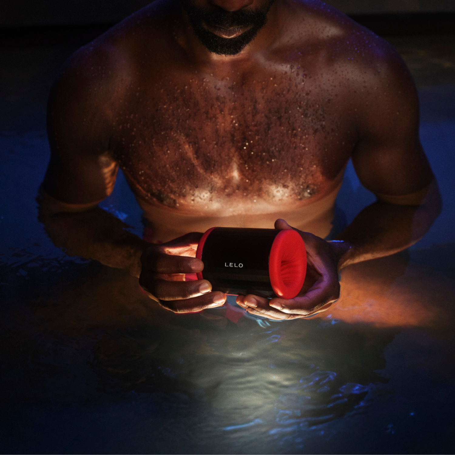 Man holding Lelo F2S red edition device in dim lighting, showing product in use.