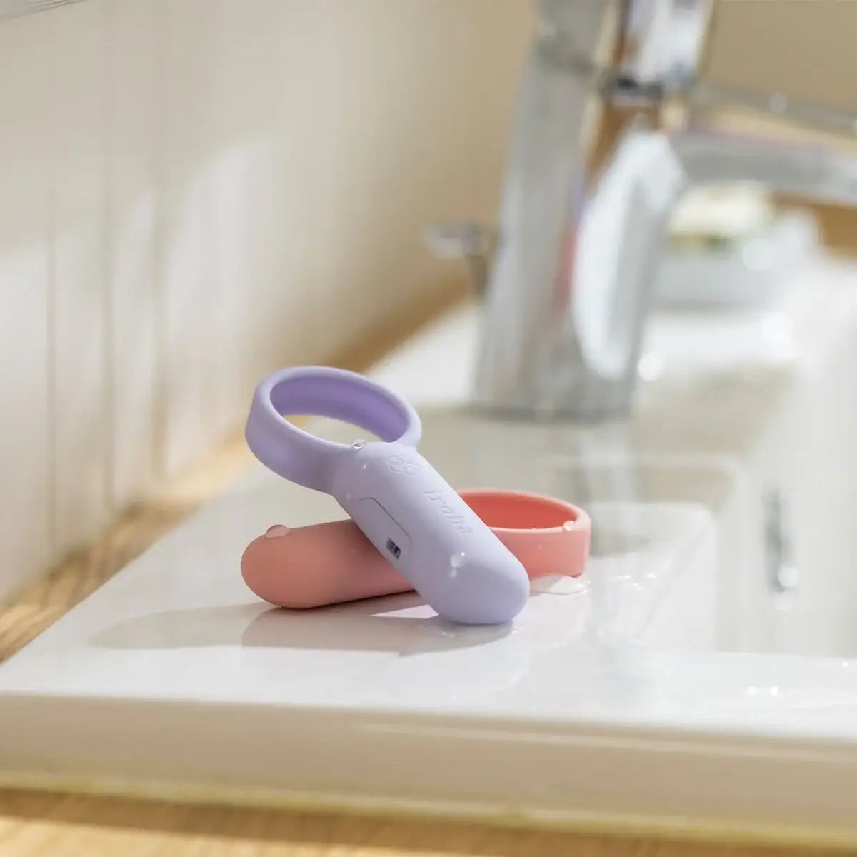 Two small electronic devices, one purple and one pink, on a bathroom counter.